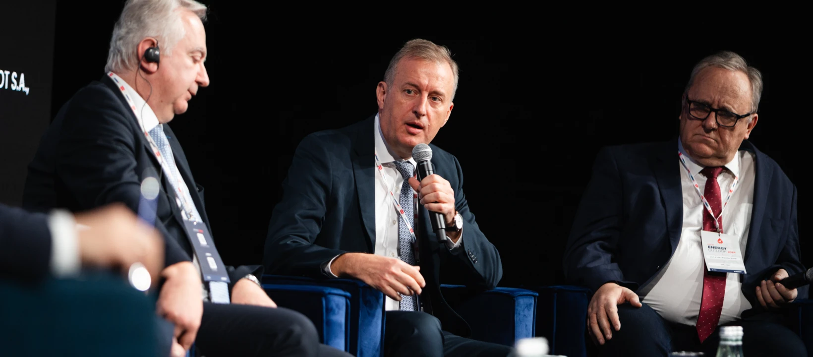 Grupa ludzi w eleganckich garniturach i płaszczach, współdziałających na wydarzeniu.