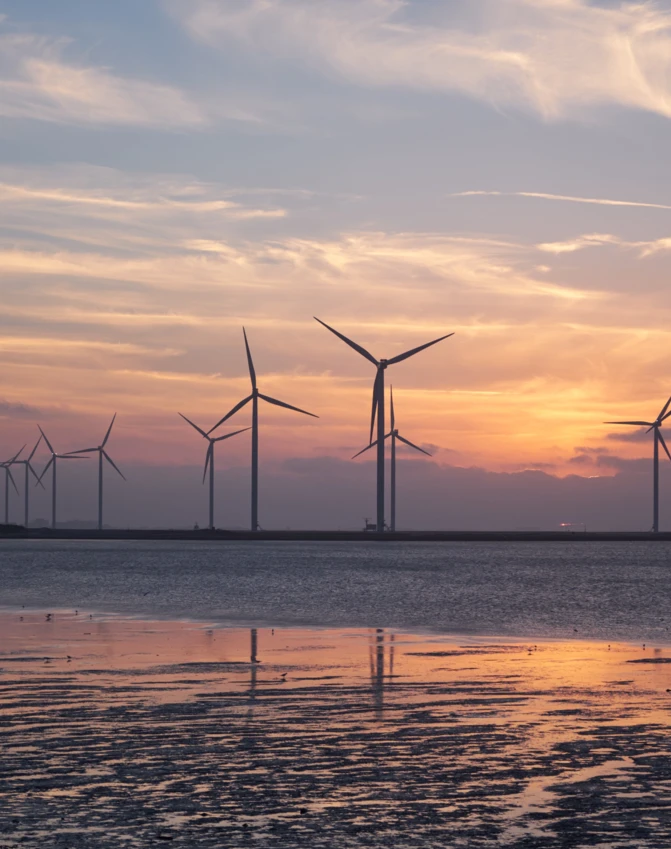 Turbina wiatrowa wznosi się wysoko na farmie wiatrowej na tle kolorowego zachodzącego nieba, z zasobami wody w tle. Spokojne światło wieczorne na horyzoncie.