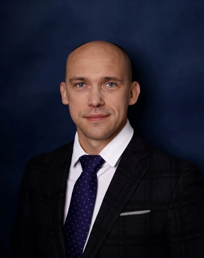 Чоловік у темно-синьому піджаку і білій сорочці з білою мандриною, демонструючи свою підборіддя, брову і лоб. Формальна одежа підкреслює його щоку, плече та шию.