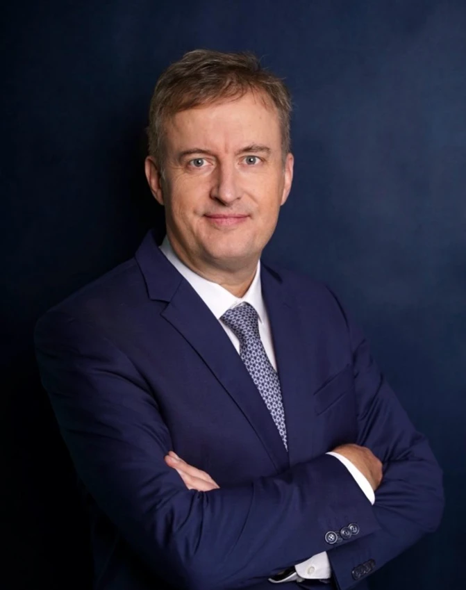 A person wearing formal clothing with styled hair and a serious expression. The focus is on their face, collar, and sleeve.