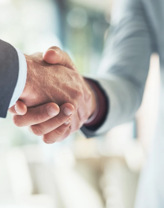 Opis obrazka: Dwóch pracowników umundurowanych w białym kolorze uściskującymi ręce w geście współpracy i wzajemnego szacunku, prezentujący znaczenie pracy zespołowej w świecie korporacyjnym.