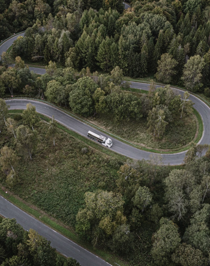 Widok z lotu ptaka na sportowe auto wykonywane na autostradzie z kontrolowanym dostępem, przecinającej bujny las, idealny na przygodę podróżną.
